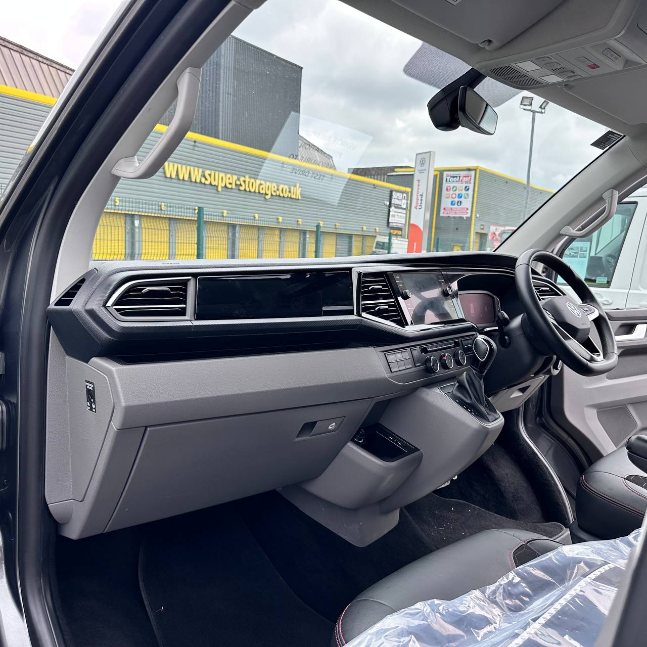 Car interior with dashboard and steering wheel, showing a Super-Storage UK building outside.