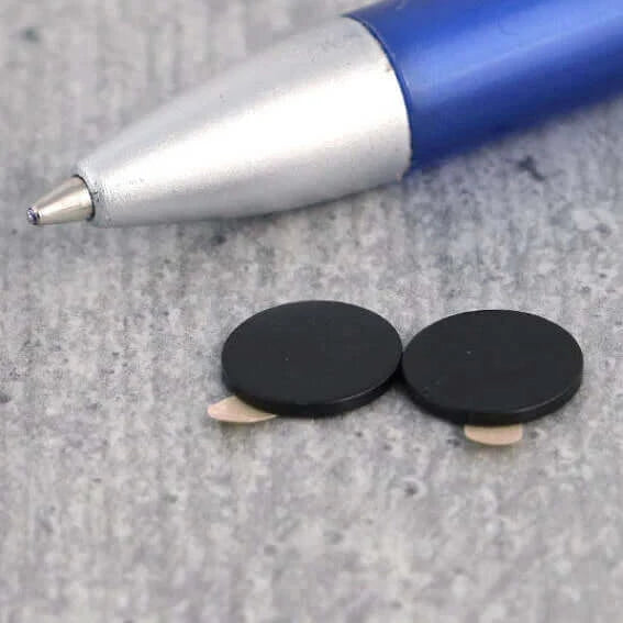 black self-adhesive neodymium disc magnets next to a pen for size compariison